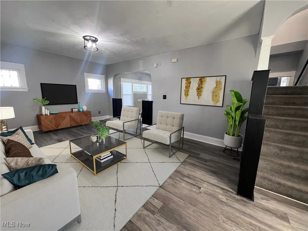Living area featuring arched walkways, stairway, wood finished floors, and a textured ceiling