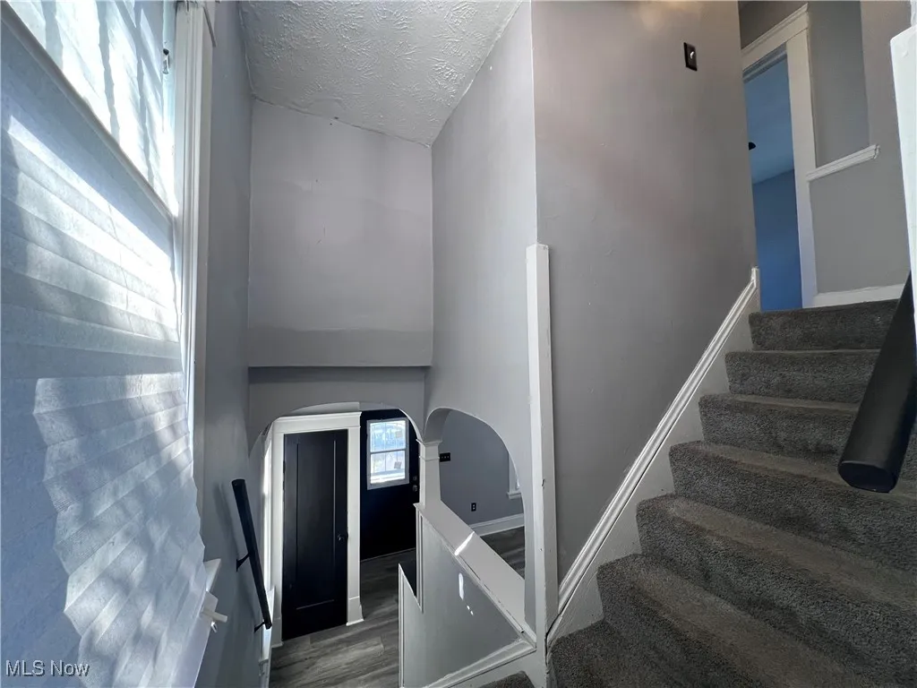 Stairway with a textured ceiling, arched walkways, wood finished floors, and a high ceiling