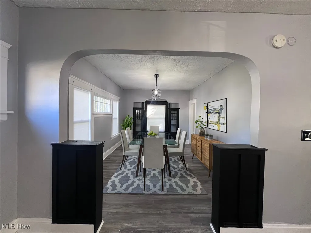 Dining area featuring arched walkways, a textured ceiling, and dark wood-style flooring