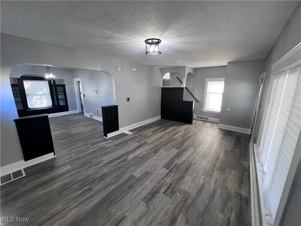 Unfurnished living room with dark wood-style floors, a textured ceiling, a chandelier, and arched walkways