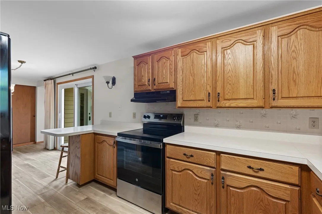 Kitchen featuring stainless steel electric range, a breakfast bar area, light countertops, a peninsula, and tasteful backsplash