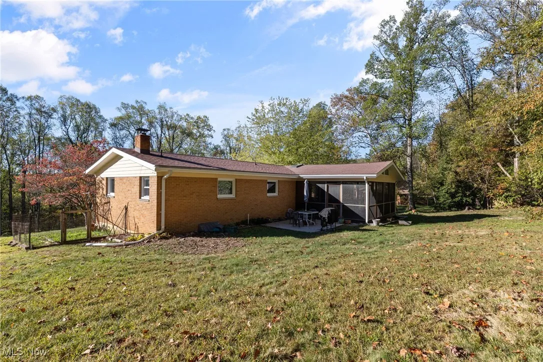 Rear view of house with a yard, brick siding, a sunroom, and a chimney