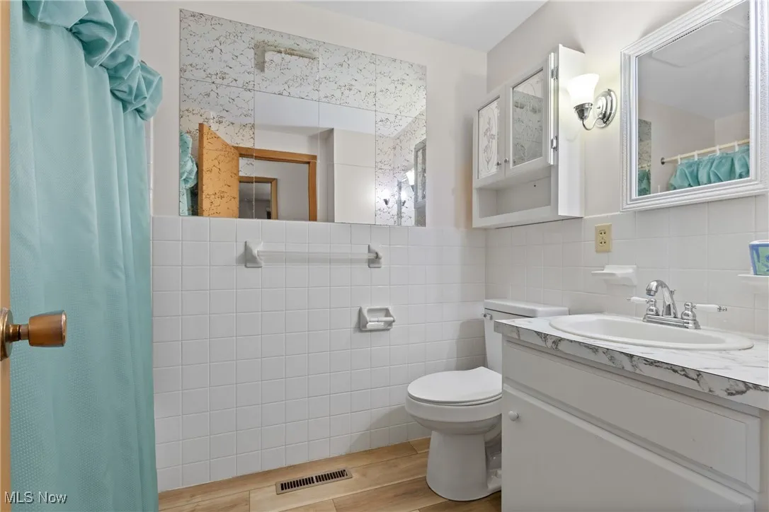 Full bathroom featuring curtained shower, tile walls, vanity, and light wood-type flooring