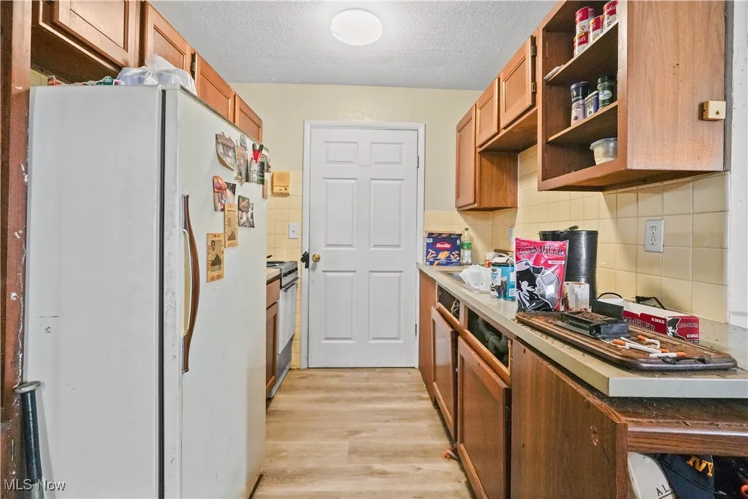 Kitchen featuring freestanding refrigerator, a textured ceiling, light wood finished floors, backsplash, and open shelves