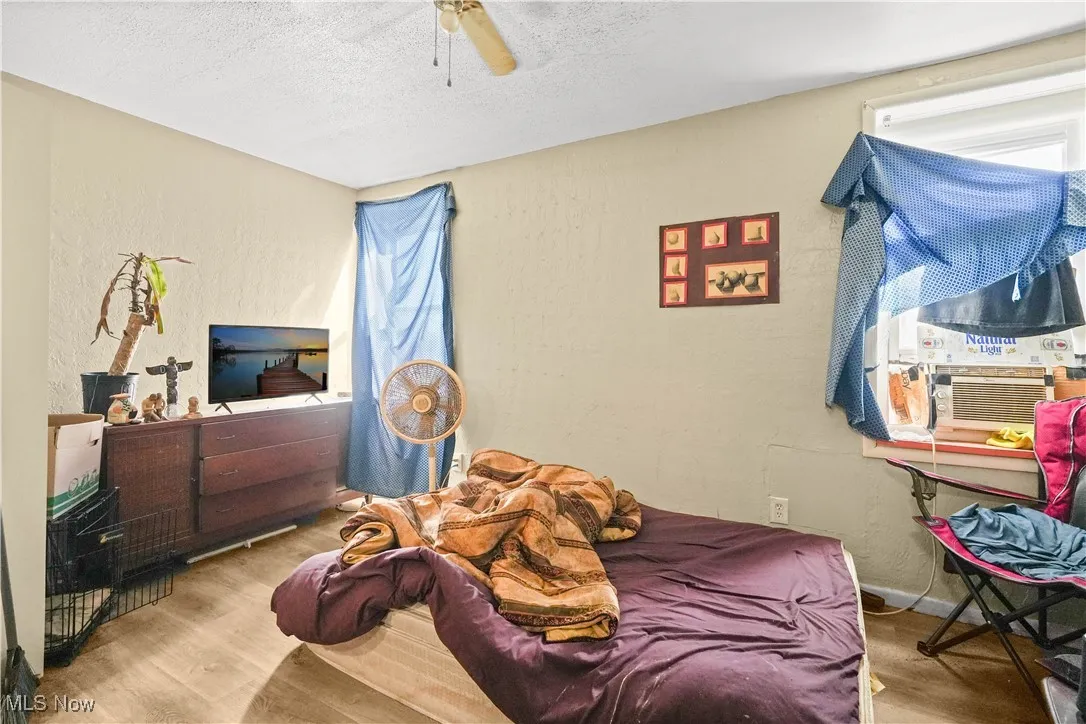 Bedroom featuring a textured wall, a textured ceiling, wood finished floors, ceiling fan, and cooling unit