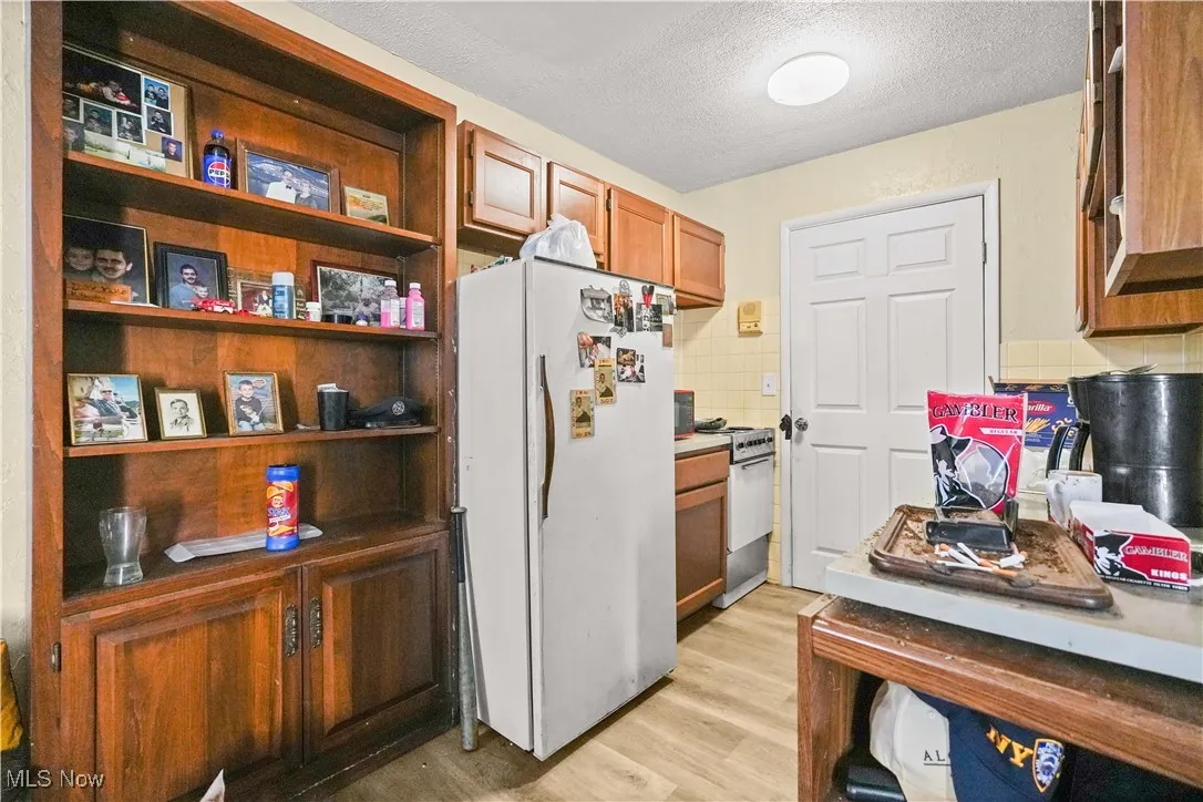 Kitchen with freestanding refrigerator, a textured ceiling, light wood-style flooring, brown cabinetry, and tasteful backsplash