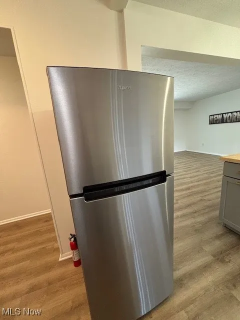 Kitchen view of freestanding refrigerator, light wood-type flooring, a textured ceiling, gray cabinets, and light countertops