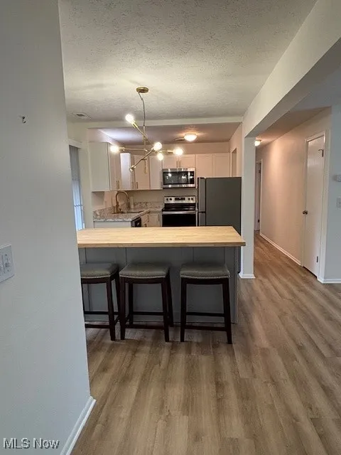 Kitchen featuring a peninsula, a kitchen bar, stainless steel range, fridge, and a textured ceiling