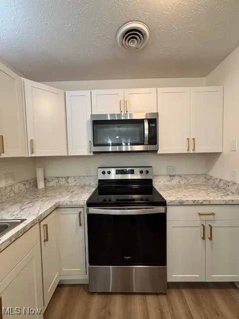 Kitchen featuring appliances with stainless steel finishes, dark wood-type flooring, white cabinets, and a textured ceiling