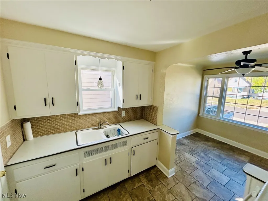 Kitchen with light countertops, decorative backsplash, white cabinetry, a ceiling fan, and plenty of natural light