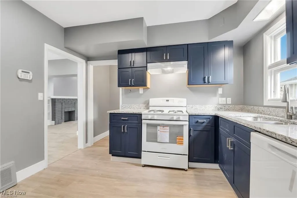Kitchen featuring white appliances, light stone counters, light wood-style floors, and under cabinet range hood