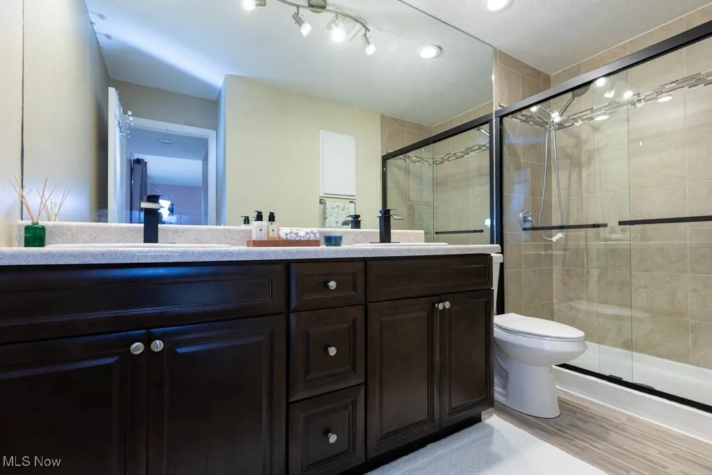 Full bathroom with double vanity, a shower stall, and light wood-type flooring