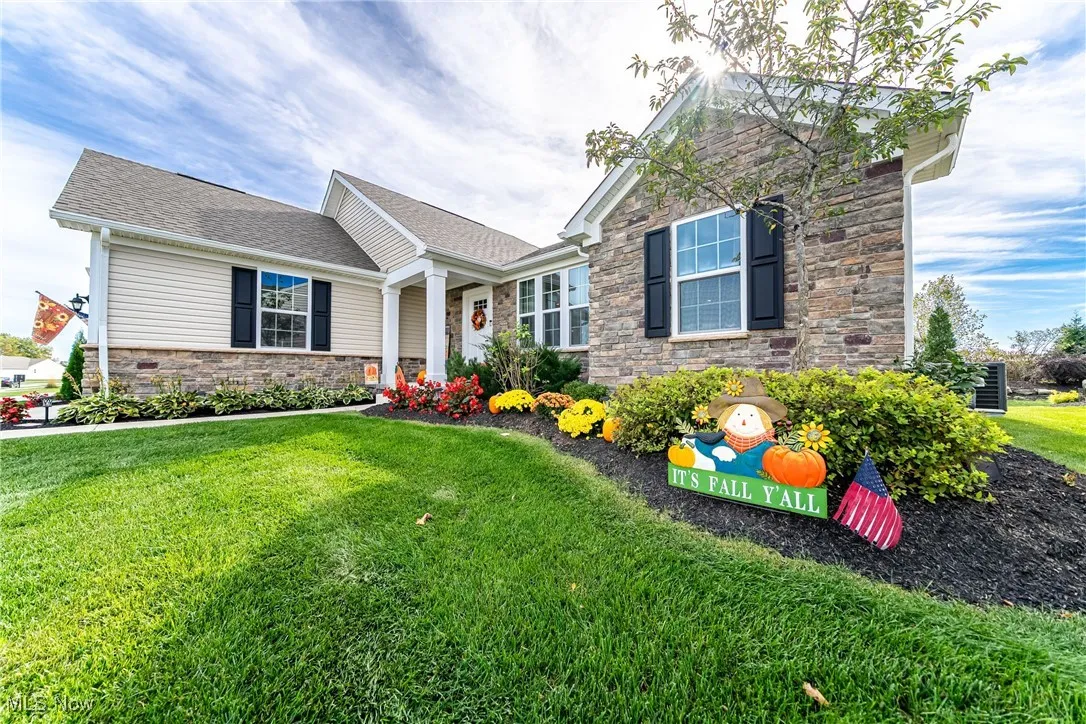 View of front facade featuring a front lawn, stone siding, and a shingled roof