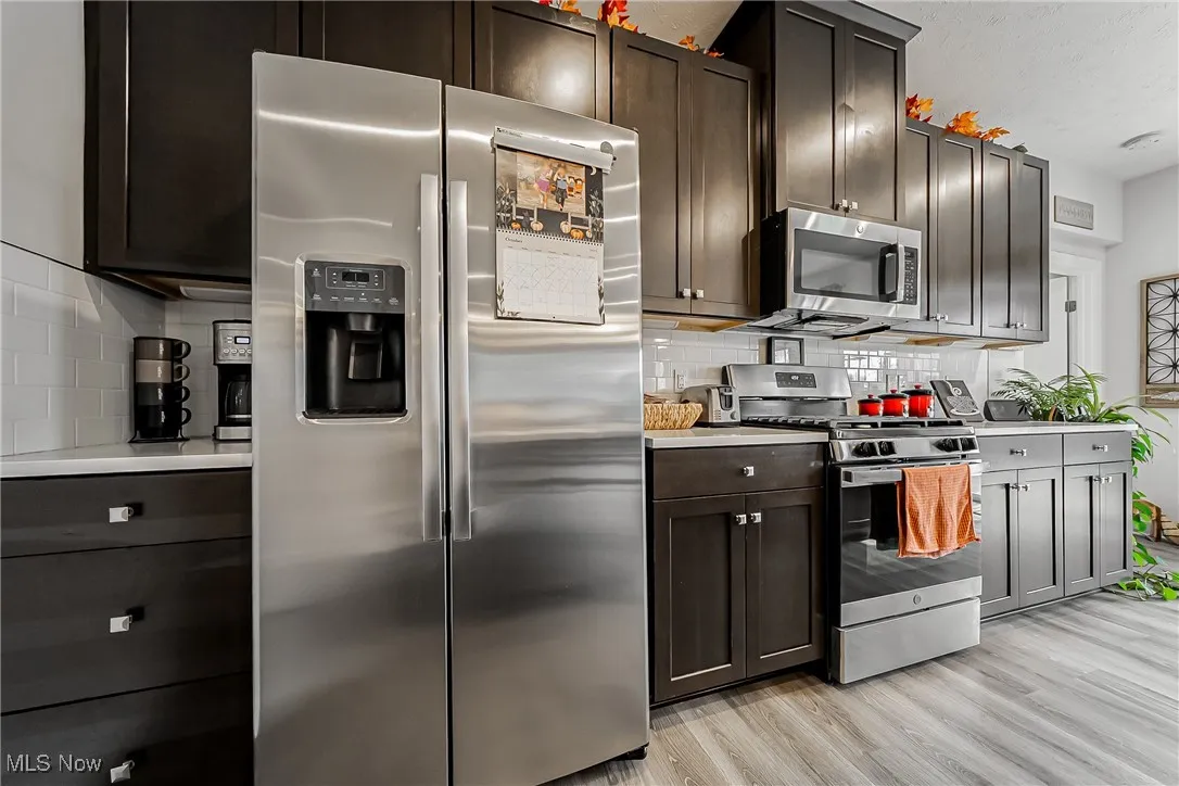 Kitchen featuring appliances with stainless steel finishes, light countertops, tasteful backsplash, light wood-style flooring, and dark brown cabinets