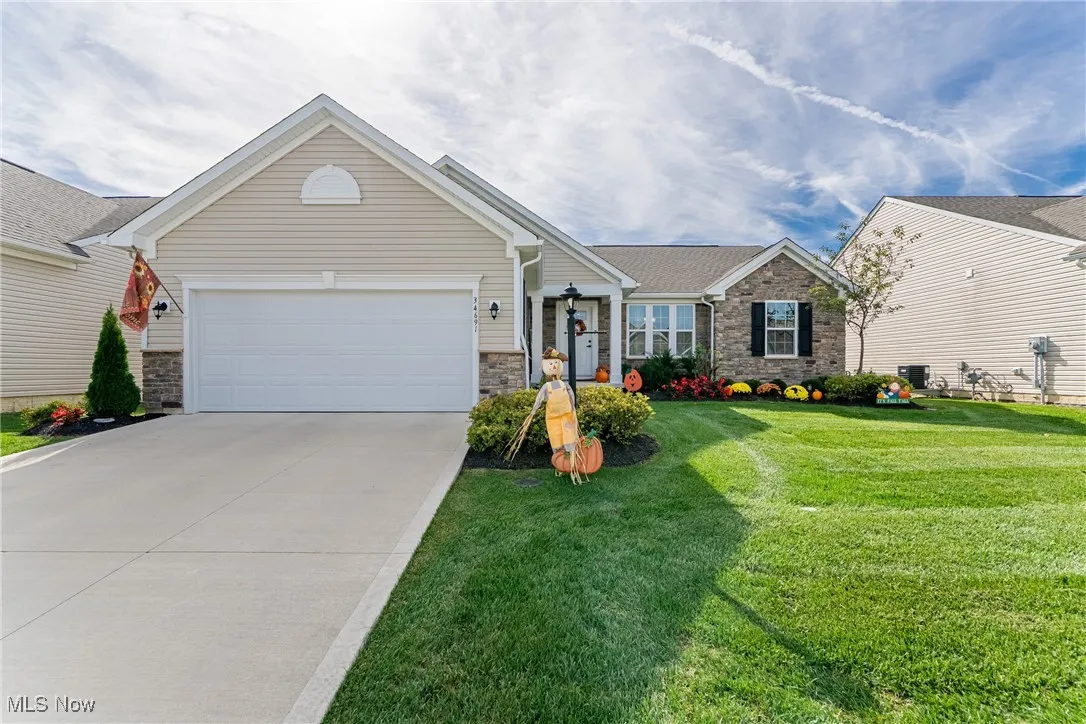 Ranch-style home featuring stone siding, driveway, a front lawn, and an attached garage