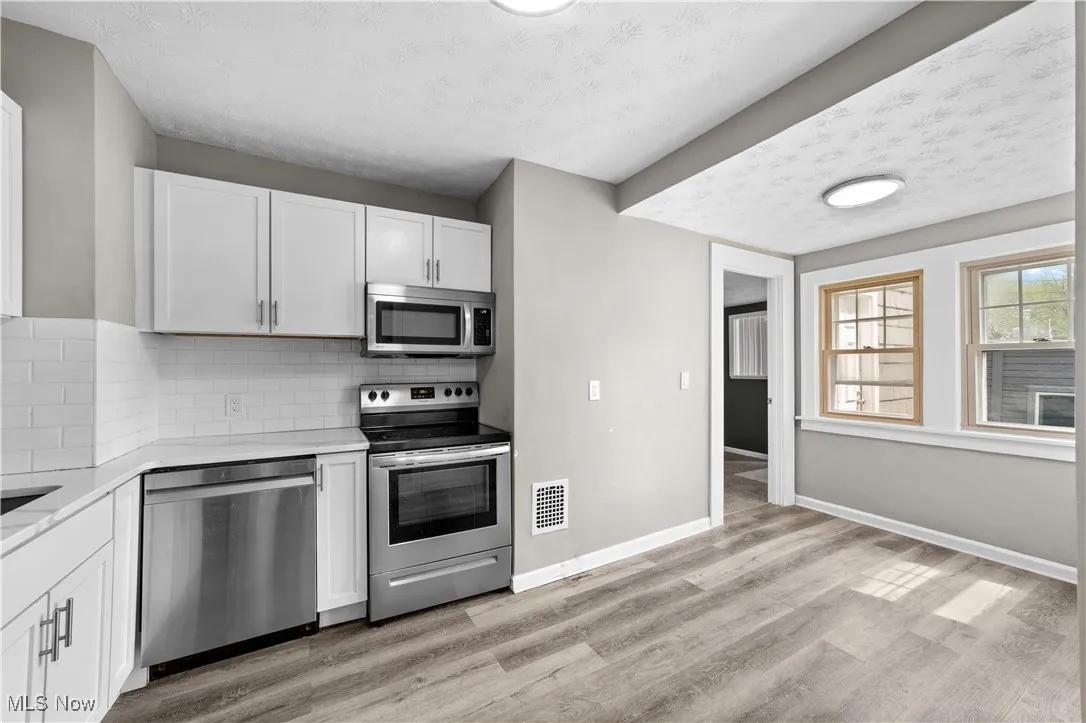 Kitchen featuring appliances with stainless steel finishes, a textured ceiling, white cabinetry, light stone countertops, and light wood-style flooring