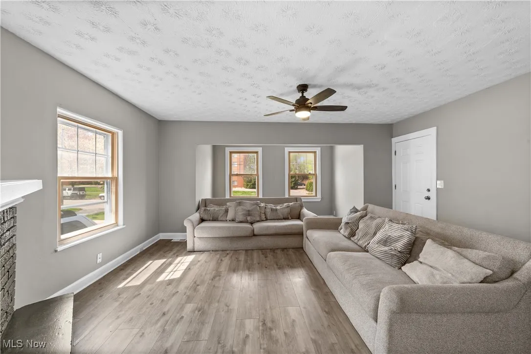 Living area with light wood-style flooring, a ceiling fan, a fireplace, and a textured ceiling