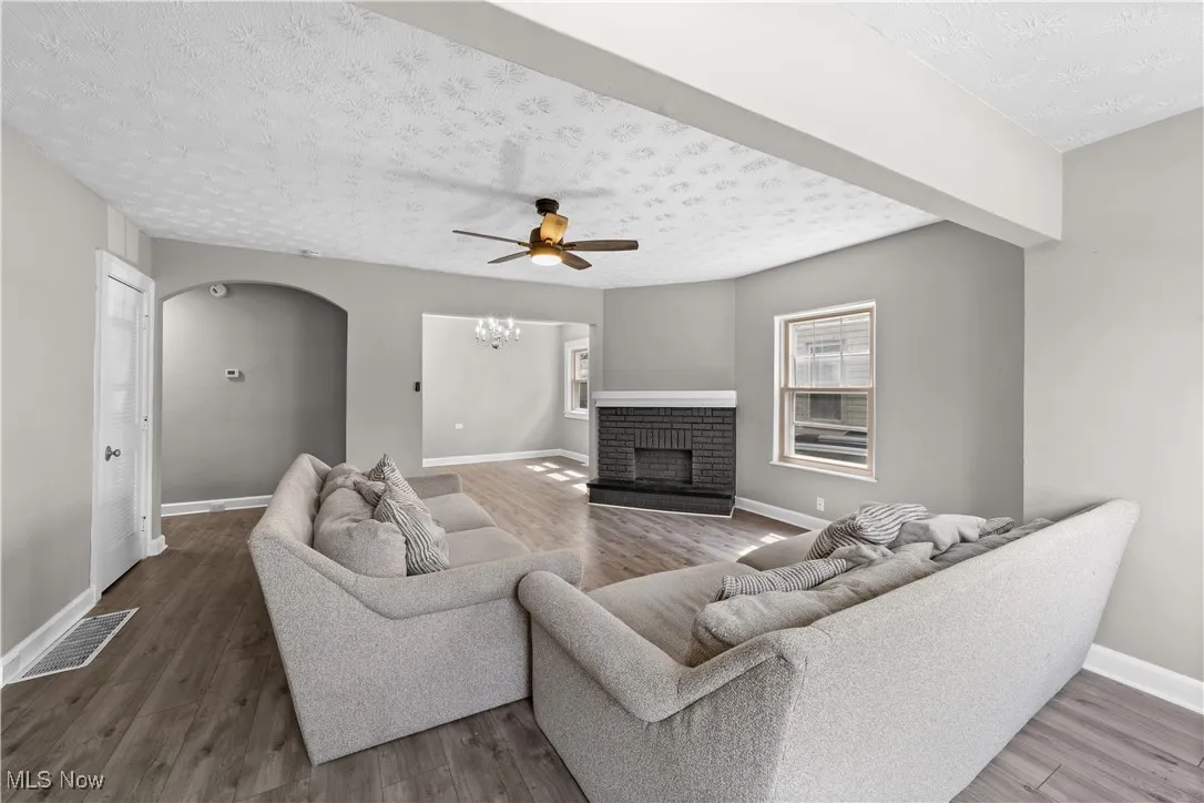 Living area with a textured ceiling, a ceiling fan, a brick fireplace, wood finished floors, and arched walkways