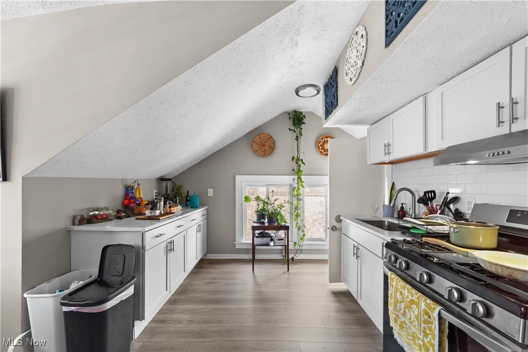 Kitchen featuring a textured ceiling, stainless steel gas range oven, white cabinets, vaulted ceiling, and under cabinet range hood