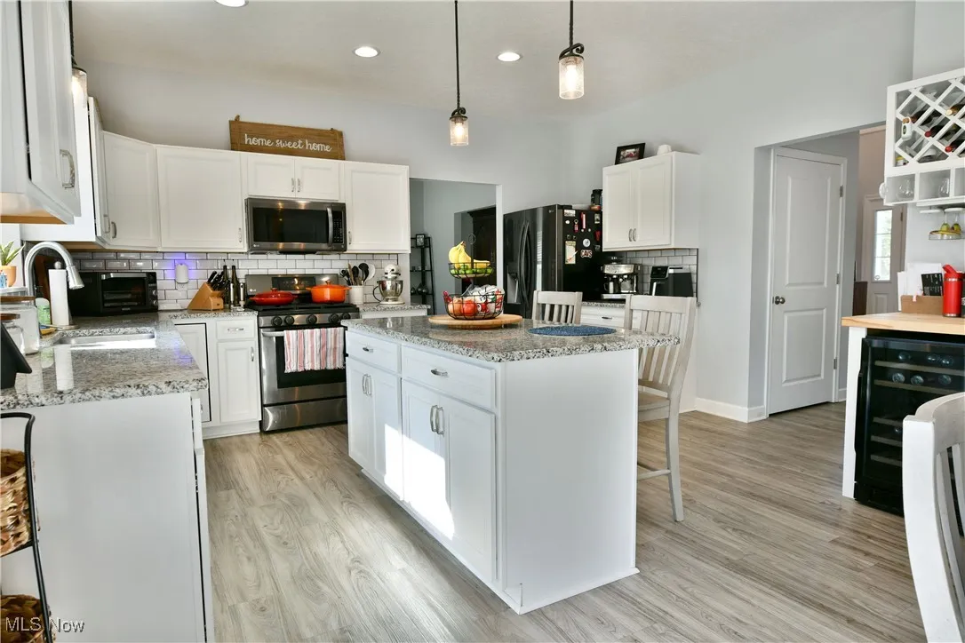 Kitchen featuring decorative backsplash, beverage cooler, appliances with stainless steel finishes, white cabinetry, and a kitchen breakfast bar