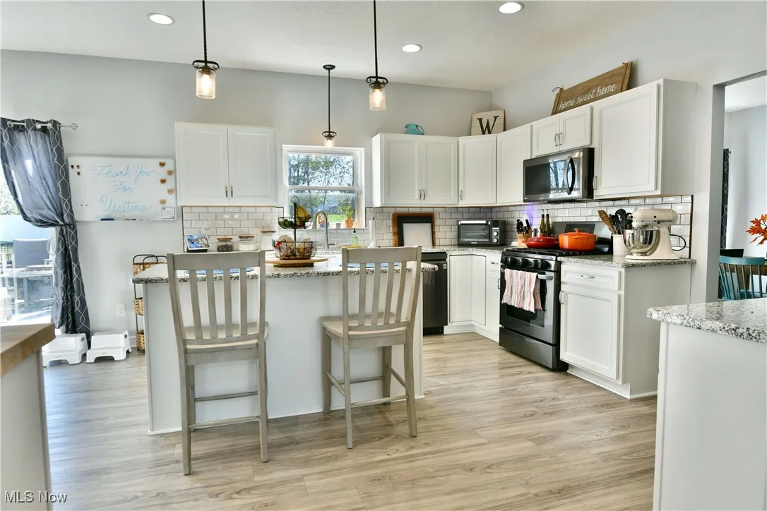 Kitchen with backsplash, pendant lighting, appliances with stainless steel finishes, white cabinetry, and light wood-type flooring