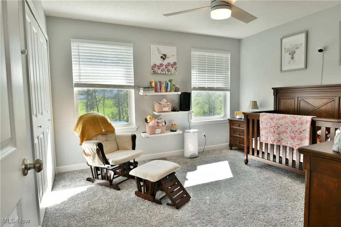 Bedroom featuring light carpet, a nursery area, and ceiling fan
