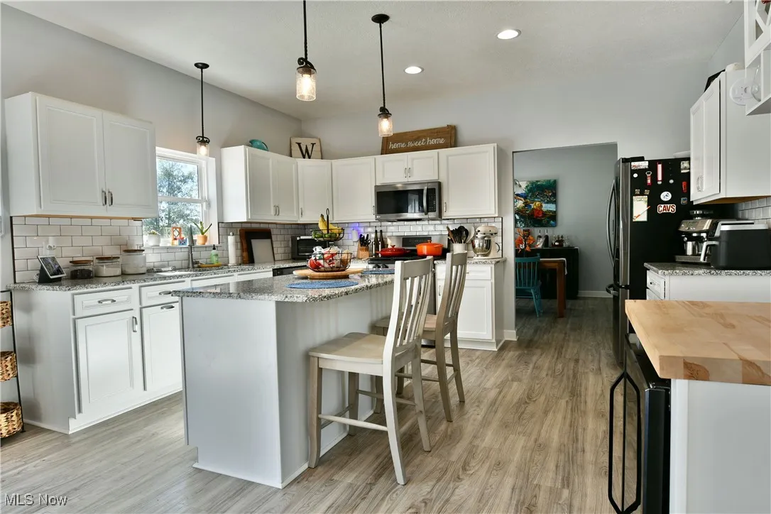 Kitchen featuring backsplash, light stone counters, pendant lighting, white cabinetry, and a breakfast bar area