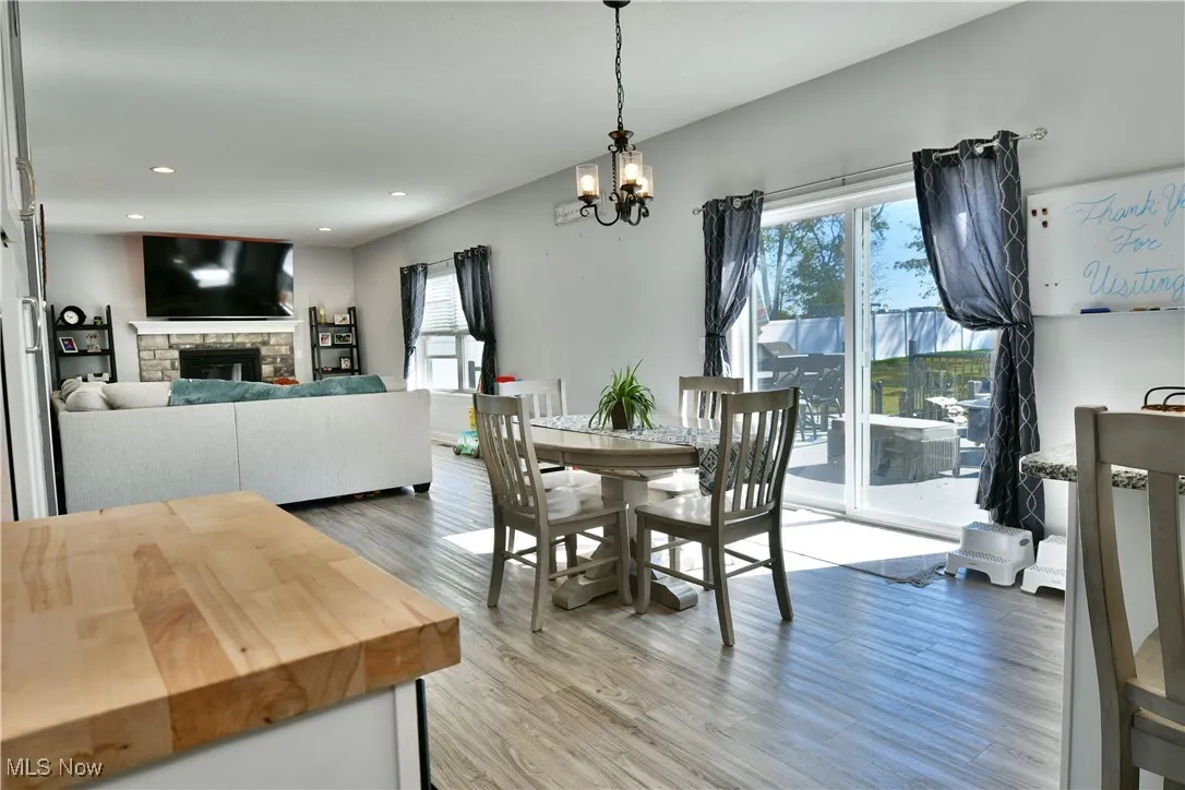 Dining area with light wood-style flooring, a stone fireplace, a chandelier, and recessed lighting