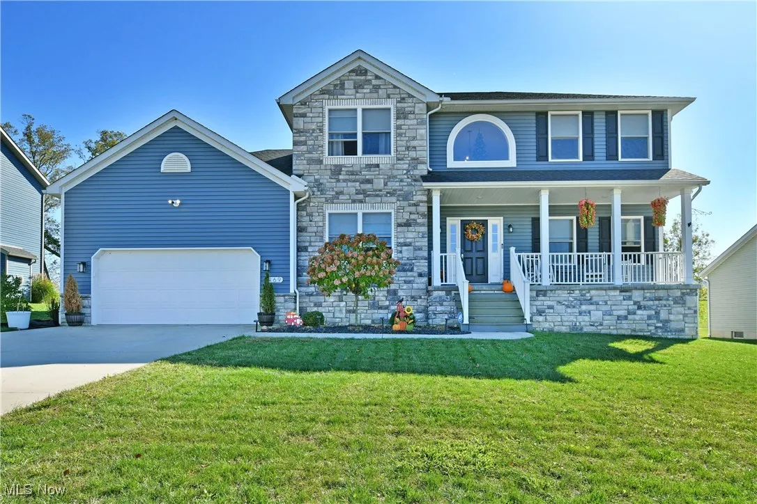 View of front of property with stone siding, covered porch, concrete driveway, and a front lawn