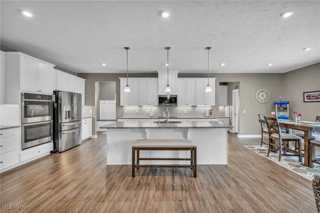 Kitchen with white cabinetry, appliances with stainless steel finishes, light wood-type flooring, recessed lighting, and a breakfast bar