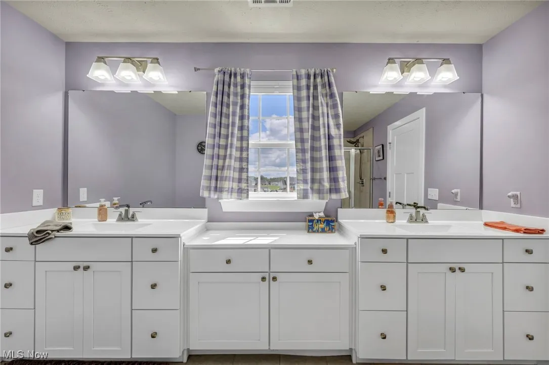Bathroom with two vanities, a textured ceiling, and light tile patterned floors