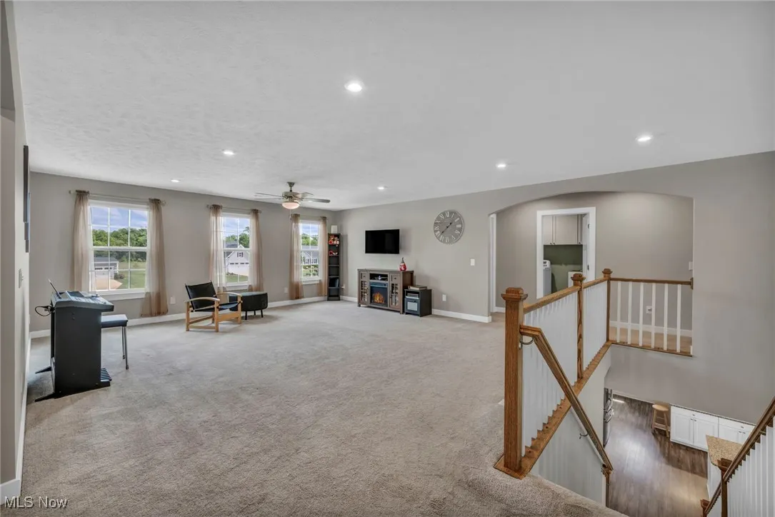 Living room with recessed lighting, carpet, a glass covered fireplace, a ceiling fan, and arched walkways