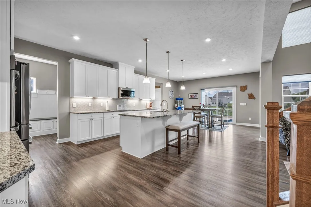 Kitchen with tasteful backsplash, a kitchen breakfast bar, light stone countertops, dark wood-style floors, and a textured ceiling