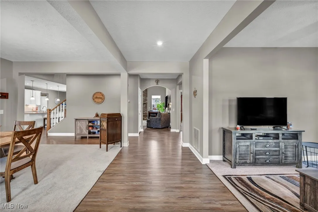 Entrance foyer featuring light wood-type flooring, arched walkways, a textured ceiling, stairway, and beamed ceiling
