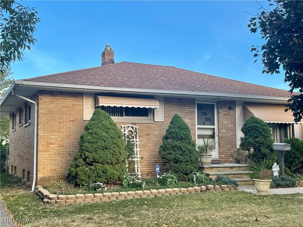 View of front of home with a front yard, brick siding, a chimney, and roof with shingles