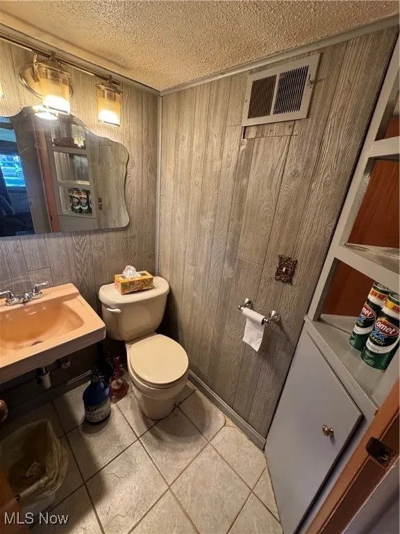Half bathroom featuring wood walls, light tile patterned flooring, and a textured ceiling