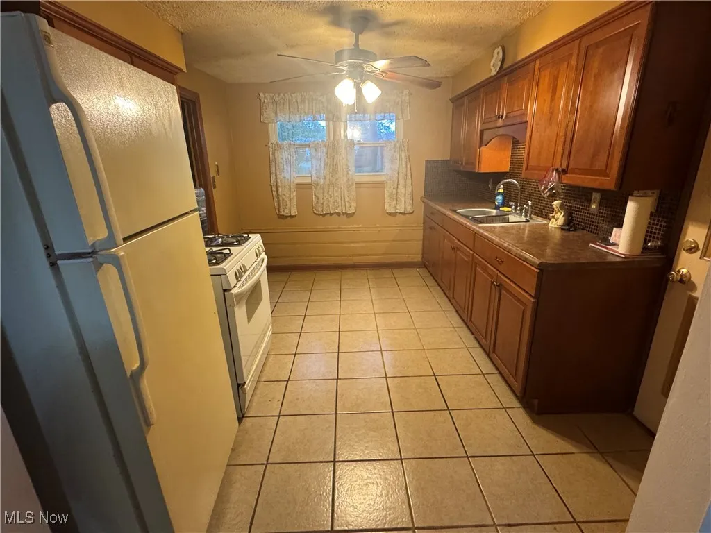 Kitchen featuring white appliances, light tile patterned floors, dark countertops, a ceiling fan, and a textured ceiling