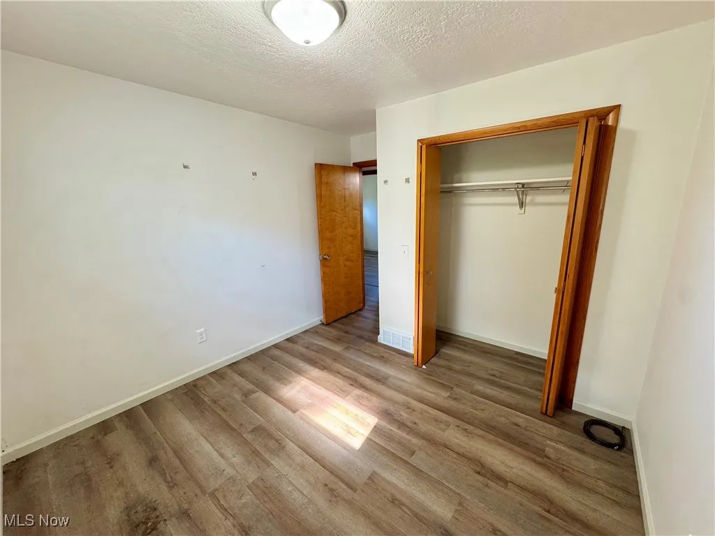 Unfurnished bedroom featuring a textured ceiling, wood finished floors, and a closet