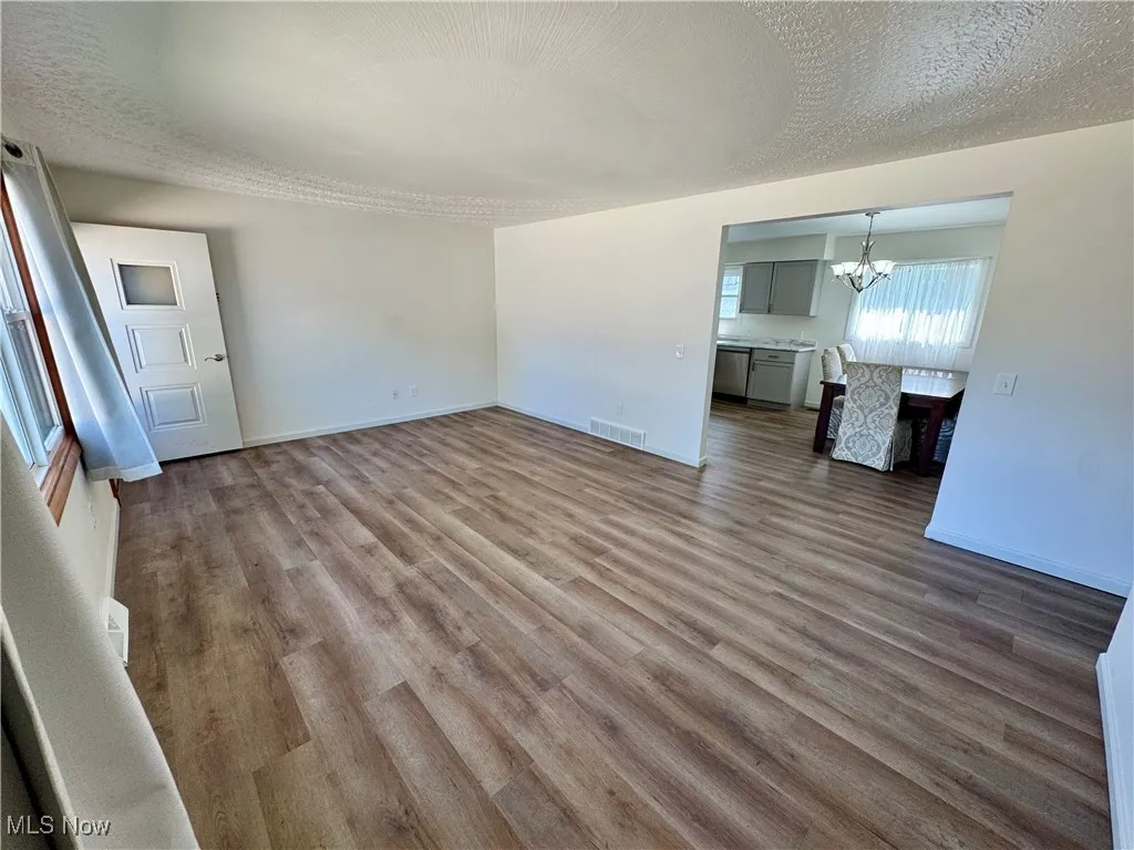 Unfurnished living room featuring a textured ceiling, dark wood-type flooring, and a chandelier