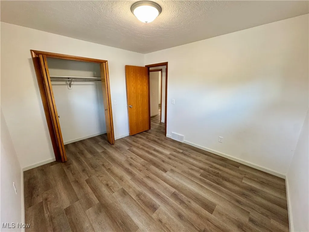Unfurnished bedroom featuring a textured ceiling, wood finished floors, and a closet