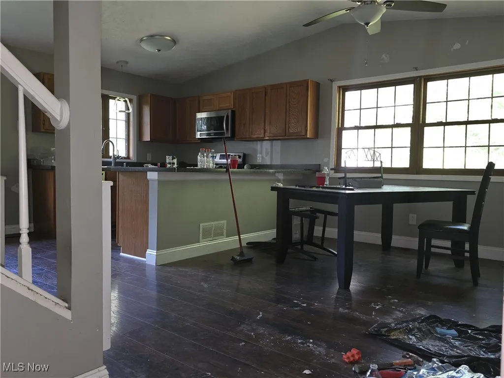 Kitchen with brown cabinets, dark wood-style flooring, stainless steel microwave, vaulted ceiling, and a ceiling fan