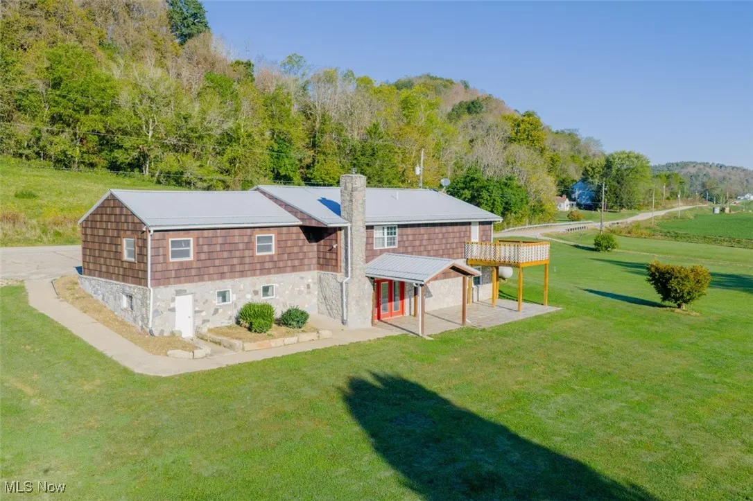 Back of property with a lawn, stone siding, a chimney, and a wooded view