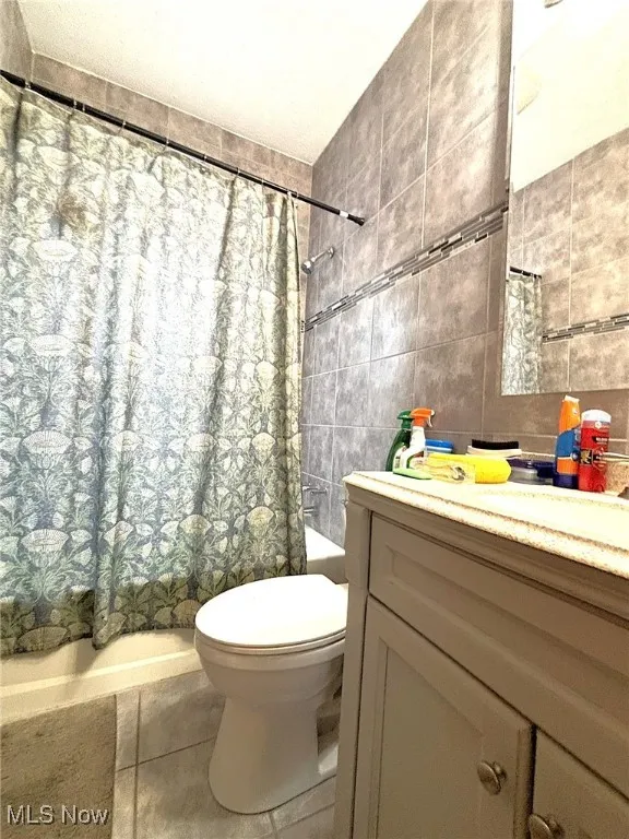 Full bath with shower / bath combo with shower curtain, tile walls, vanity, and tile patterned flooring