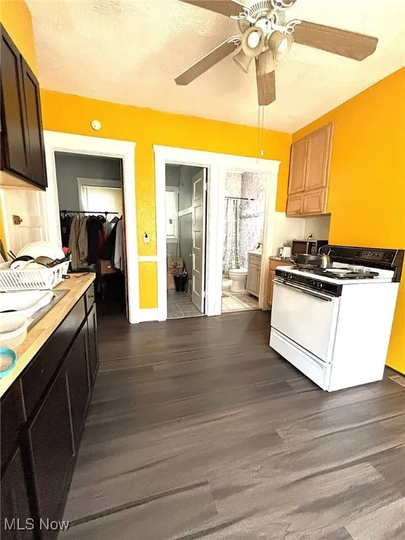 Kitchen with gas range gas stove, dark wood-style flooring, a textured ceiling, ceiling fan, and light countertops