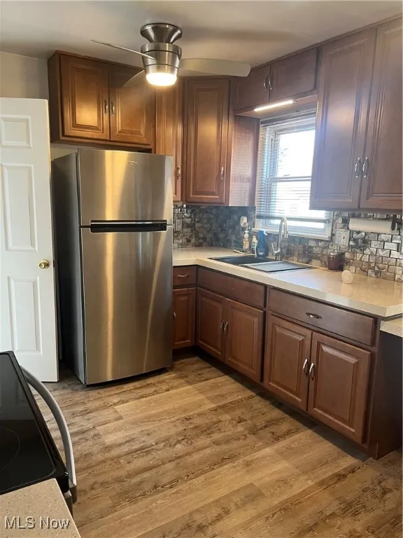 Kitchen with freestanding refrigerator, stove, light wood-type flooring, tasteful backsplash, and brown​​‌​​​​‌​​‌‌​‌‌​​​‌‌​‌​‌​‌​​​‌​​ cabinets