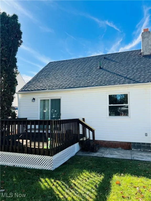Back of house with a deck, a shingled roof, a yard, and a chimney