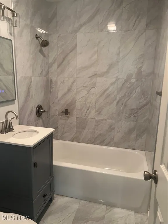 Bathroom with washtub / shower combination, vanity, and light marble finish floors