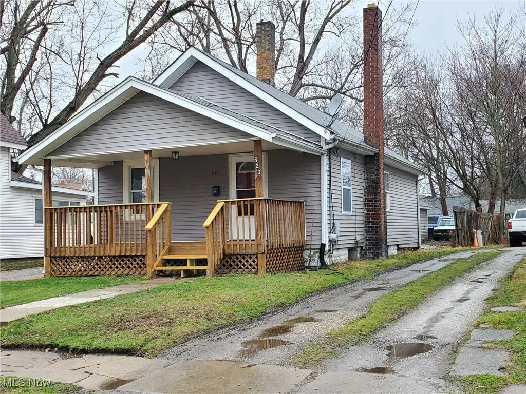 Bungalow-style home featuring a chimney, a front lawn, covered porch, and driveway