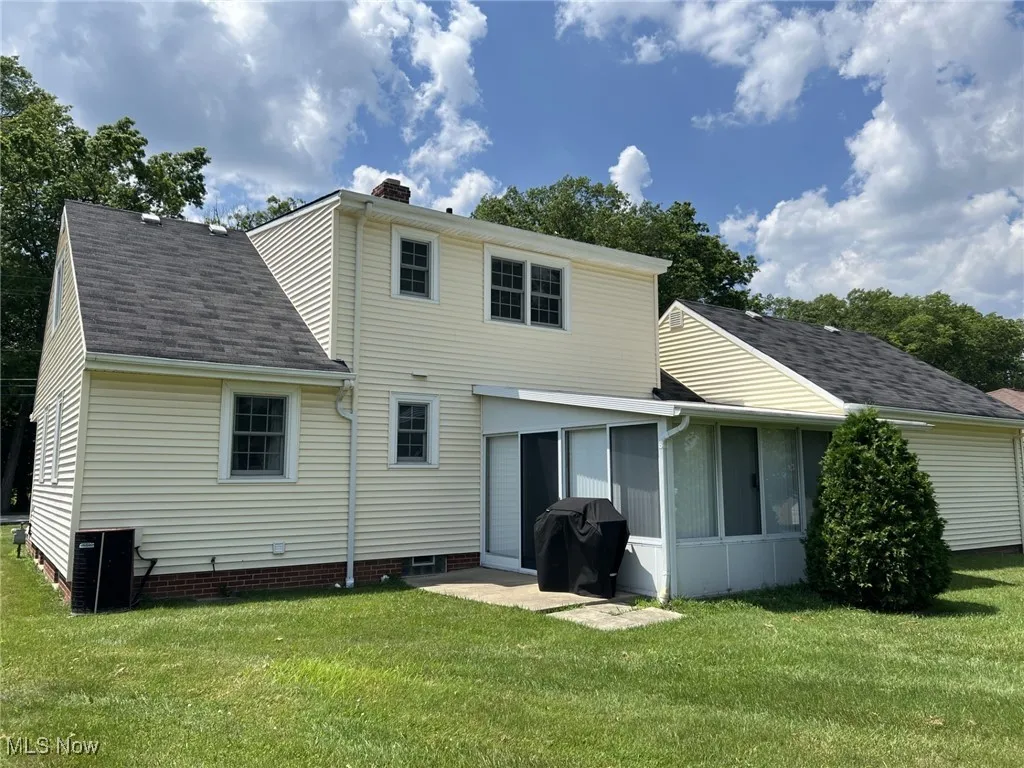 Rear view of property with roof with shingles, a sunroom, a yard, and a chimney