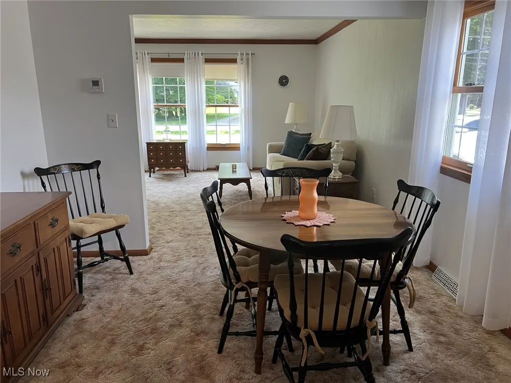 Dining space with light carpet, healthy amount of natural light, and crown molding
